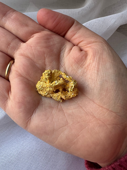 Hand holding a large gold nugget against a light background